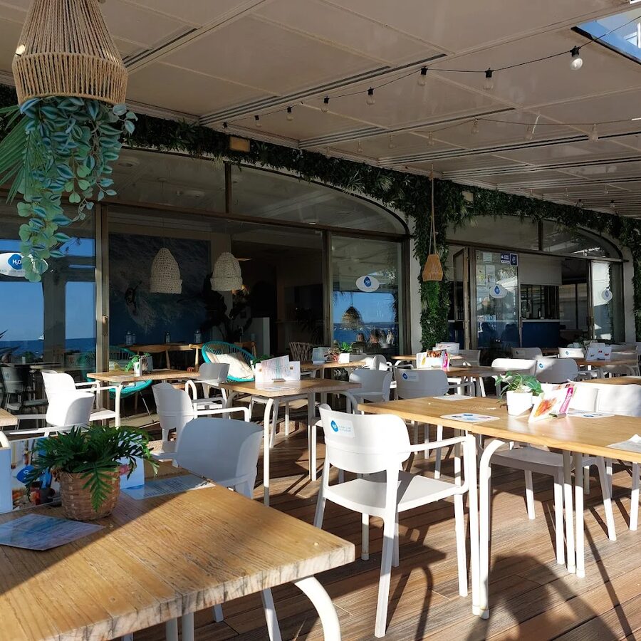 Terraza del restaurante con mesas blancas, plantas colgantes y vistas al mar
