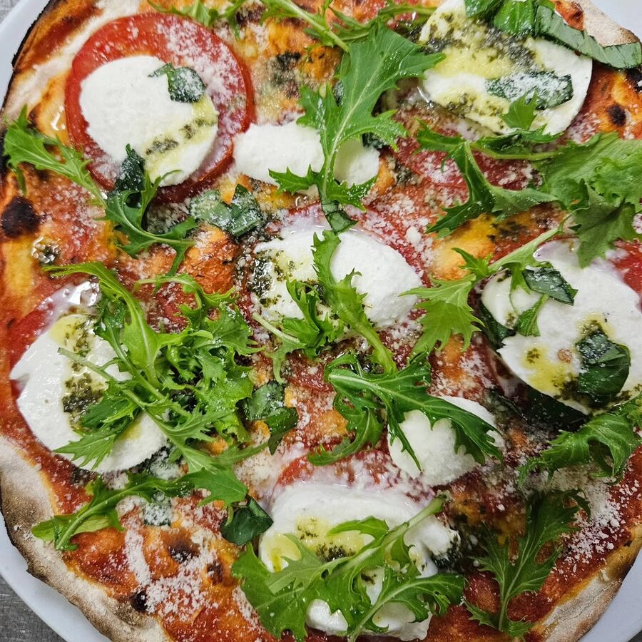 Pizza con mozzarella, tomate, rúcula y pesto recién horneada