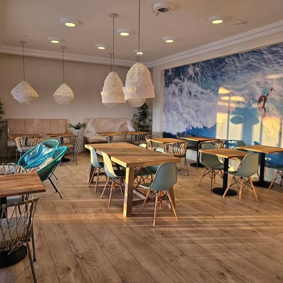 Sala interior con sillas de diseño, mesas de madera y mural de surf